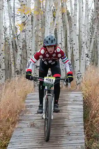 Silver Creek male athlete descends off a bridge with fall colors in the background at Granby Ranch
